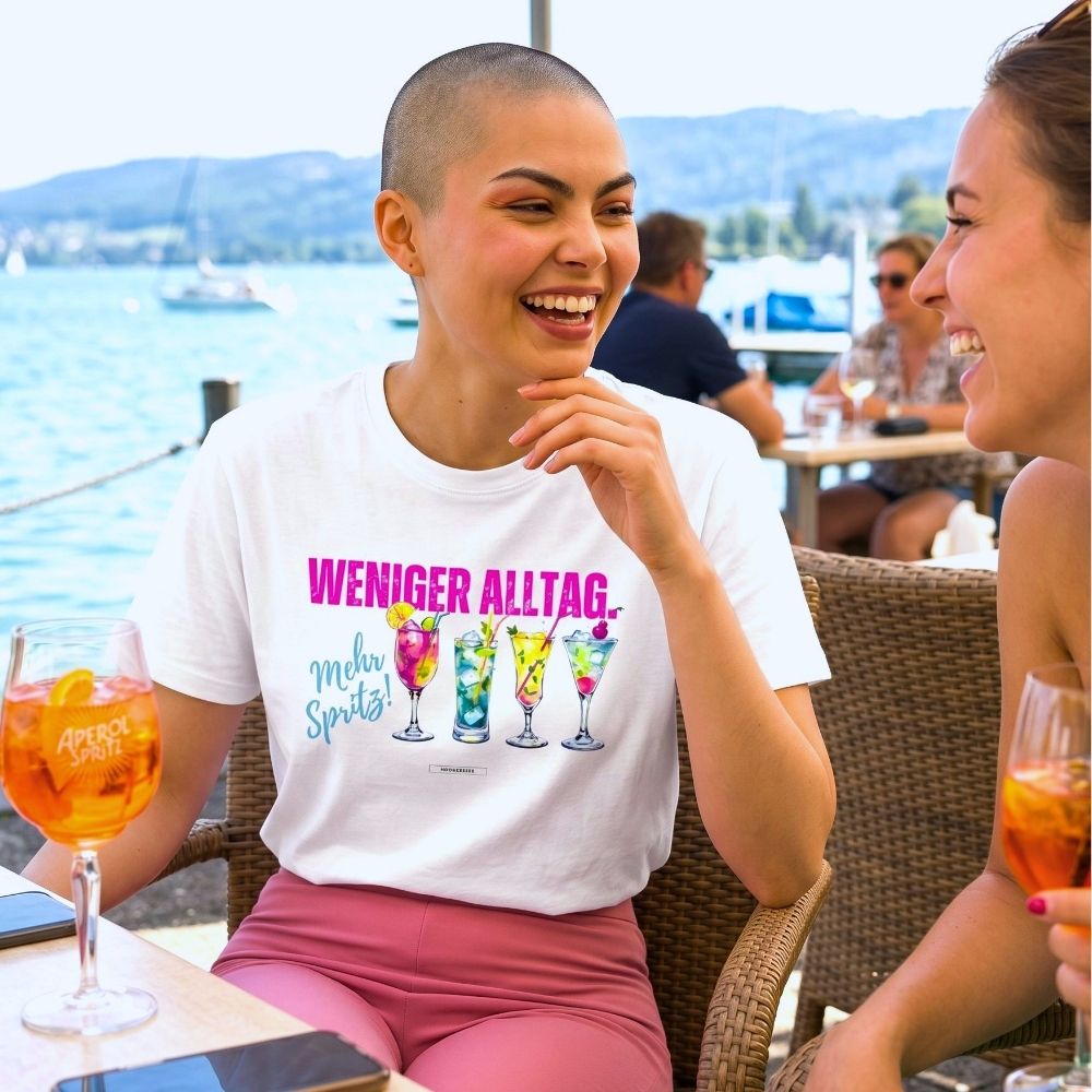     Weißes Statement-Shirt mit Cocktail-Motiv und pinkem Schriftzug beim Aperitif am Wasser getragen.