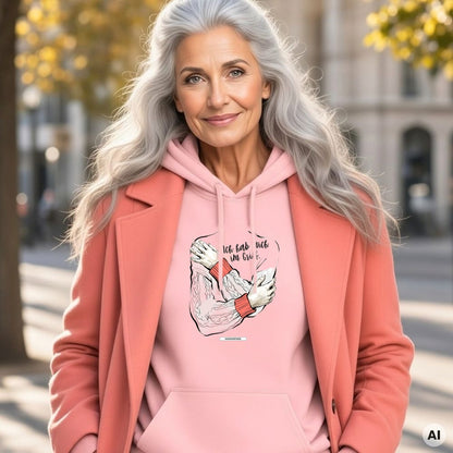 Frau mit langen grauen Haaren und korallfarbenem Mantel trägt den HOOKamSEE Hoodie Ich hab mich im Griff. in Hellrosa auf einer herbstlichen Straße