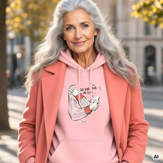 Frau mit langen grauen Haaren und korallfarbenem Mantel trägt den HOOKamSEE Hoodie Ich hab mich im Griff. in Hellrosa auf einer herbstlichen Straße