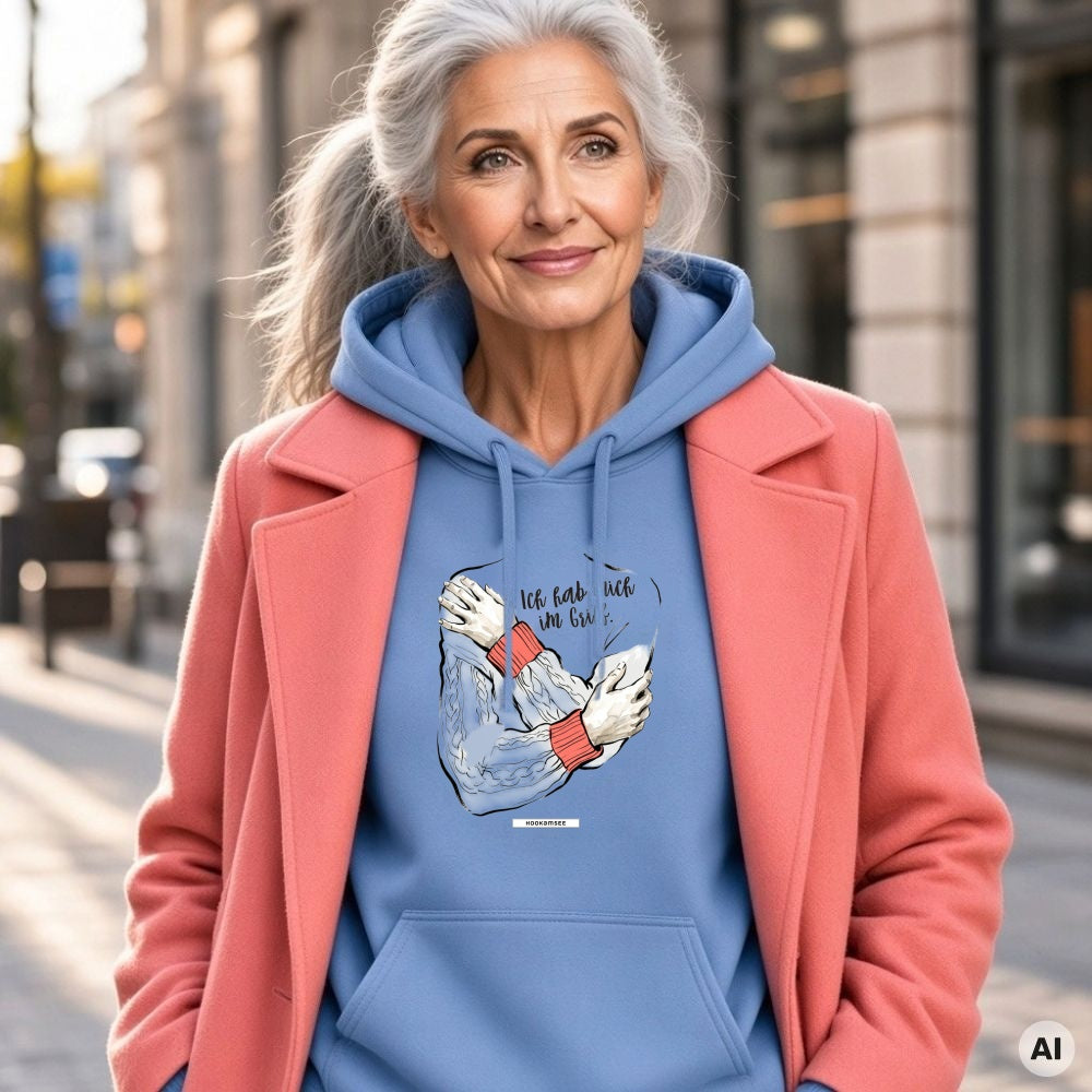 Frau mit grauem Pferdeschwanz und korallfarbenem Mantel trägt den HOOKamSEE Statement-Hoodie Ich hab mich im Griff. in Carolina Blue in der Stadt