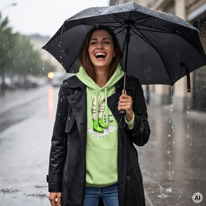 Lachende Frau mit schwarzem Trenchcoat und Regenschirm trägt den HOOKamSEE Hoodie Ich tanze auch im Regen. in Pistazie im Regen auf einer nassen Straße