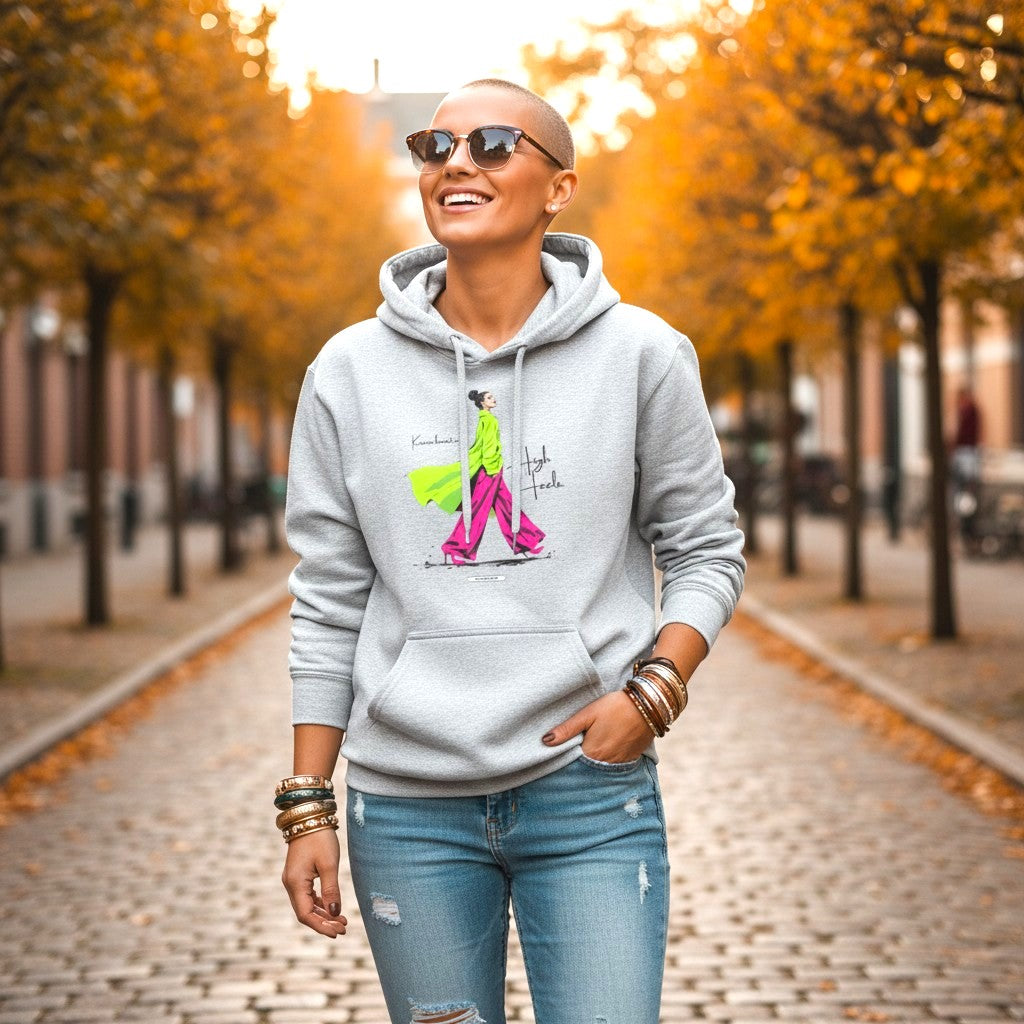 Frau mit kurzem, blondem Haar trägt HOOKamSEE Hoodie Karma kommt auf High Heels in Hellgrau meliert, herbstliche Allee mit gelb-orangem Laub im Hintergrund