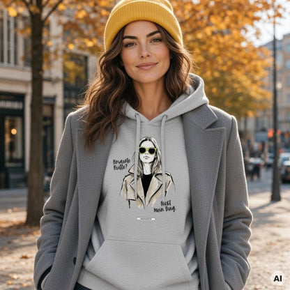 Frau mit gelber Beanie und langen braunen Wellen in grauem Hoodie mit Illustration, dazu grauer Wollmantel, auf einer Straße im Herbstlicht
