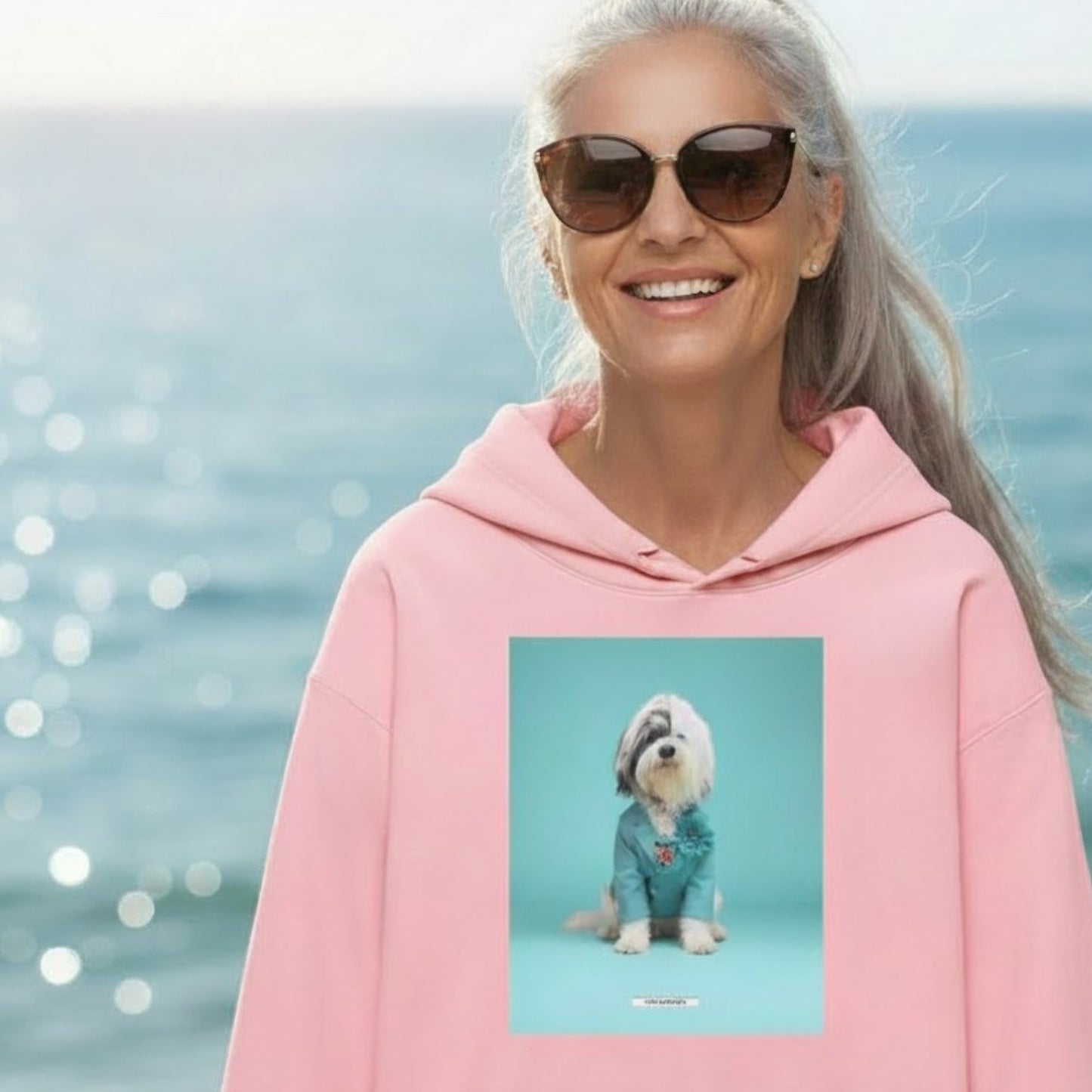 Lachende Frau mit Sonnenbrille trägt den HOOKamSEE Hoodie Styled Dogs Tibet-Terrier in Hellrosa am Wasser