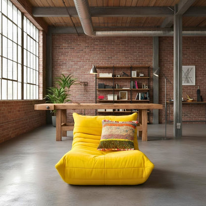 Kissen Amber Harvest auf einem gelben Loungesessel vor einem Holztisch in einem Loft mit Backsteinwand.