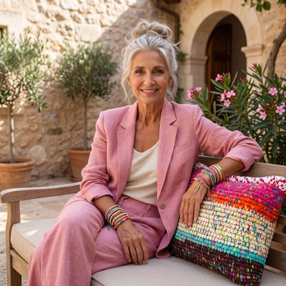 Frau in rosafarbenem Blazer sitzt auf Bank neben Kissen Confetti Horizon in mediterranem Innenhof
