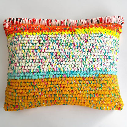 Coiled-Crochet-Kissen Golden Carnival 55×45 cm mit Farbverlauf von Orange über Neon-Gelb zu cremeweißem Konfetti-Muster und Senfgelb-Ocker, oberer Rand mit Kante aus rot-weiß-schwarzen Stoffstreifen, freigestellt auf hellgrauem Hintergrund