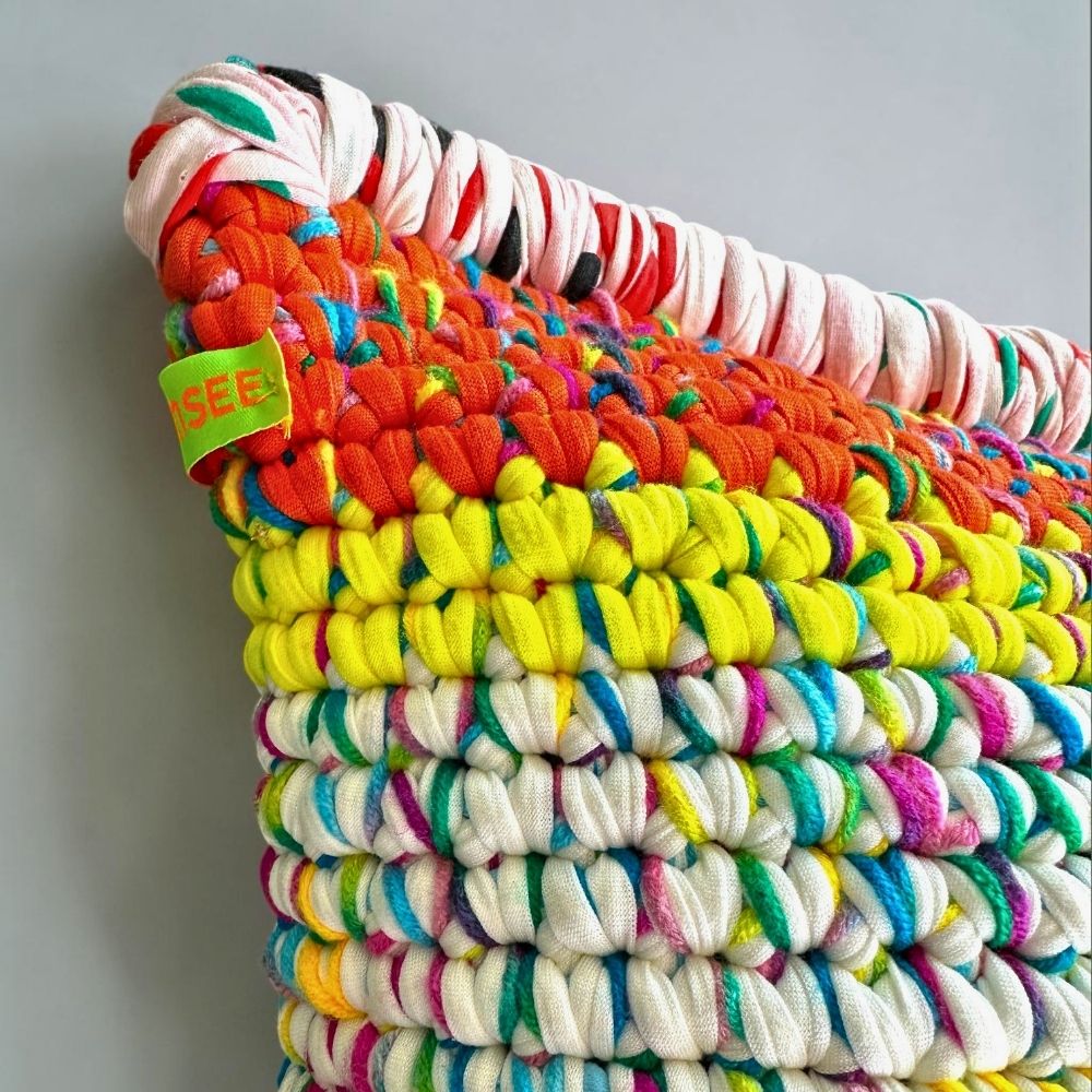 Detailaufnahme der Stoffstreifen-Kante und der orange-gelben Coiled-Crochet-Reihen von Kissen Golden Carnival mit sichtbarem HOOKamSEE-Label