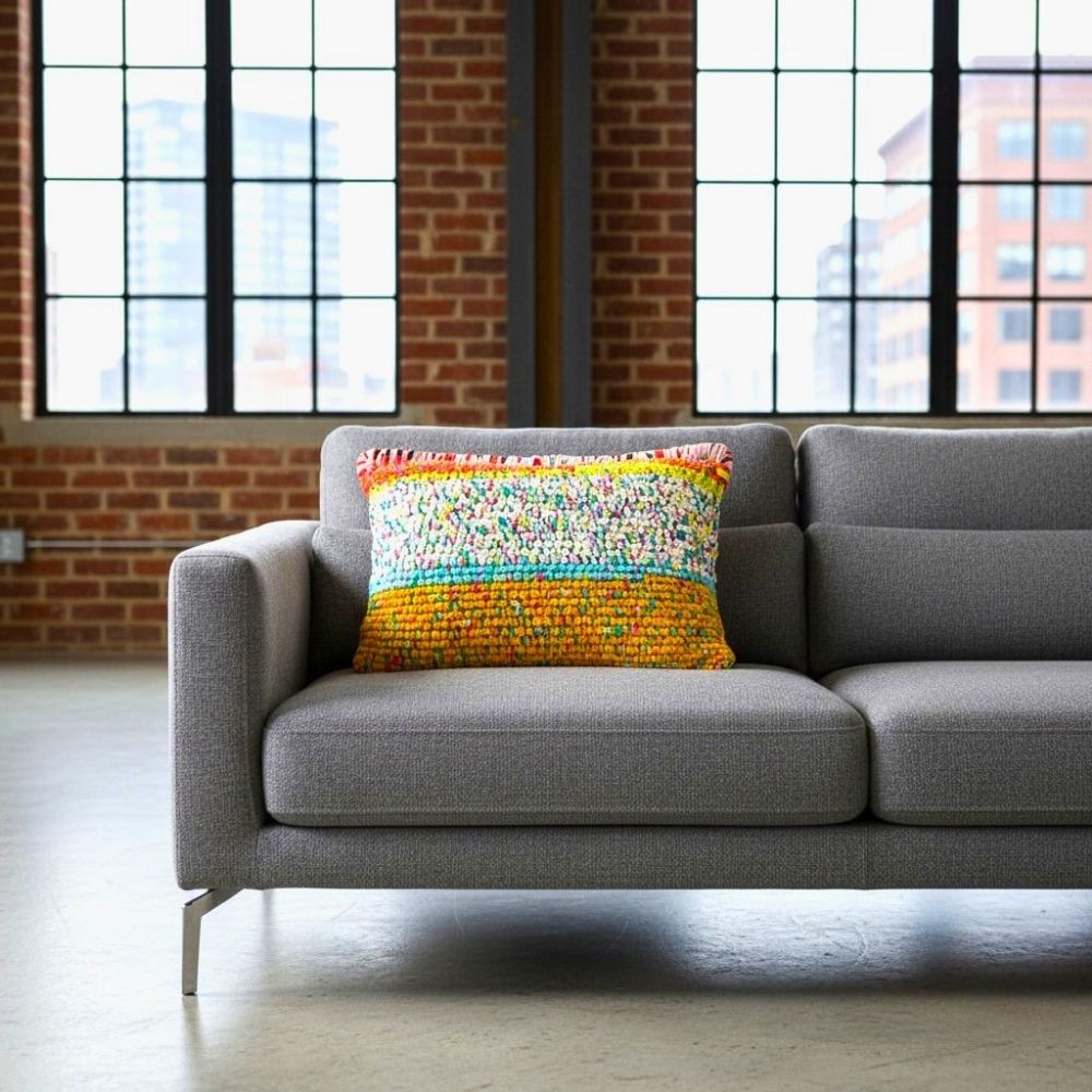 Kissen Golden Carnival auf einem grauen Loungesofa in einem Loft mit Backsteinwand und großen Sprossenfenstern
