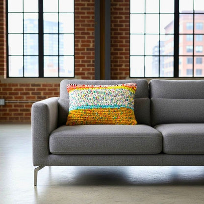 Kissen Golden Carnival auf einem grauen Loungesofa in einem Loft mit Backsteinwand und großen Sprossenfenstern