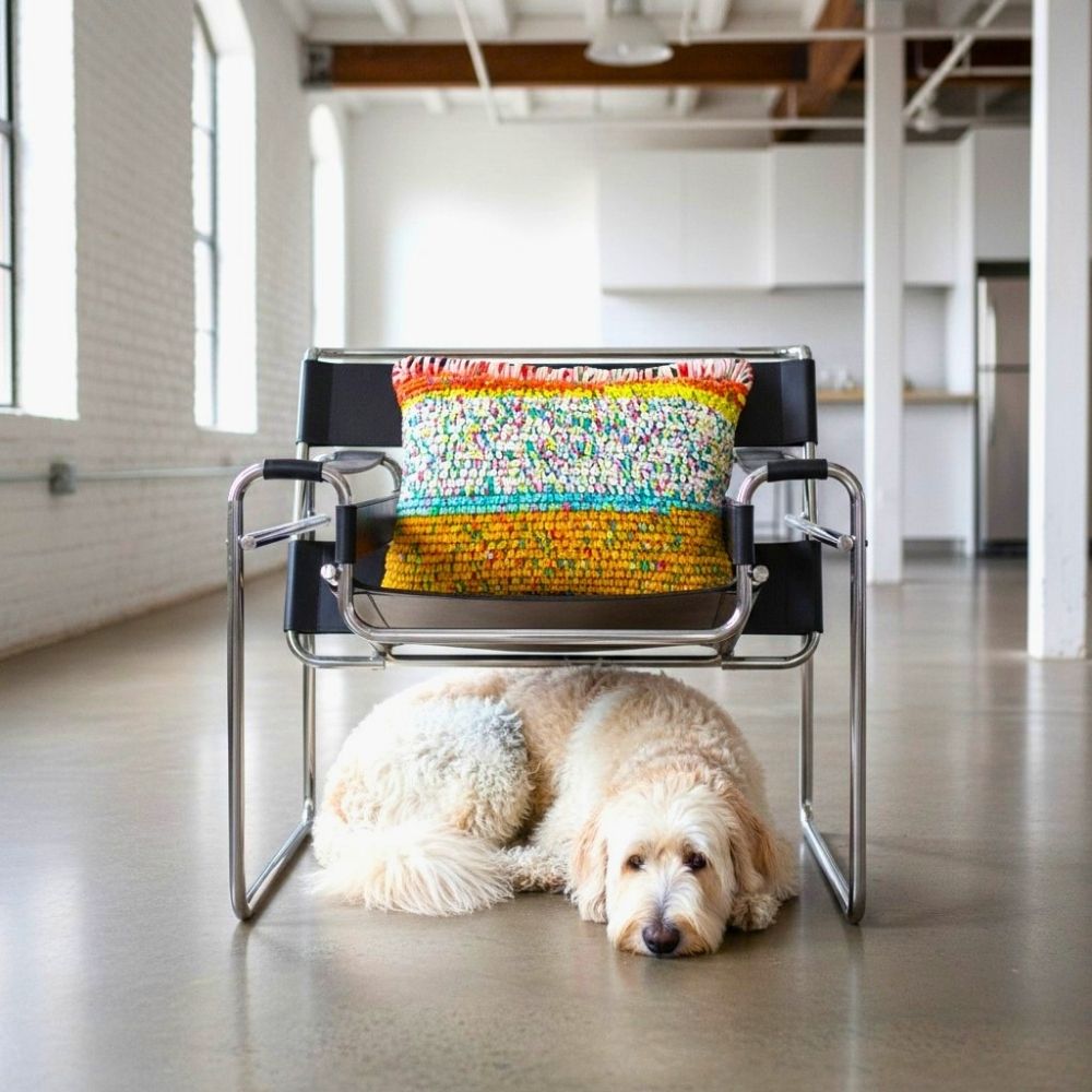 Kissen Golden Carnival auf einem Wassily Chair, davor liegt ein Goldendoodle auf dem Boden eines hellen Loftraums
