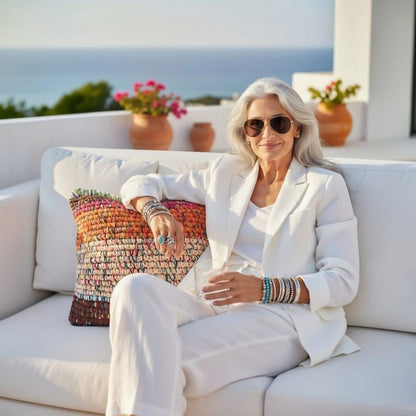 Frau in weißem Anzug auf Terrassensofa mit Meerblick, Kissen Rust Blossom als Akzent im Hintergrund