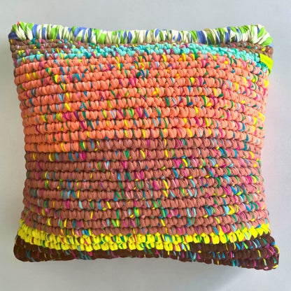 Coiled-Crochet-Kissen Terracotta Ember 45×45 cm mit Farbverlauf von Koralle-Apricot über Terracotta-Rosébraun zu Kastanienbraun, oberer Rand mit grün-blau-weißer Bändchengarn-Kante, freigestellt auf hellgrauem Hintergrund