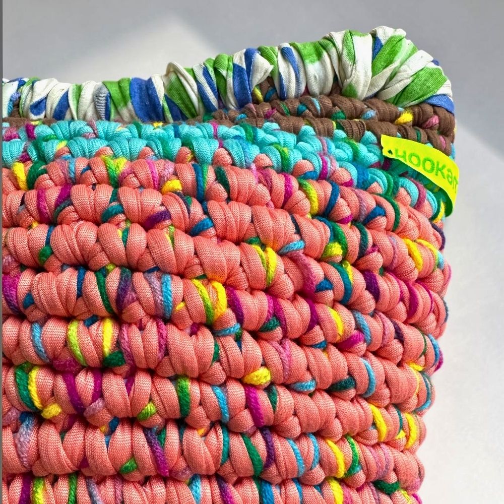 Nahaufnahme der grün-blau-weißen Bändchengarn-Kante von Kissen Terracotta Ember mit HOOKamSEE-Markenlabel in Neon-Gelb
