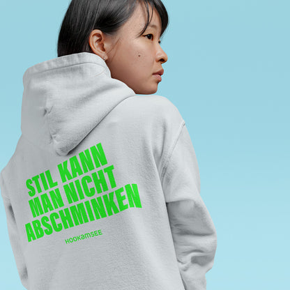 Frau trägt weißen Unisex Hoodie mit grünem Rückenprint „STIL KANN MAN NICHT ABSCHMINKEN“ von HOOKamSEE